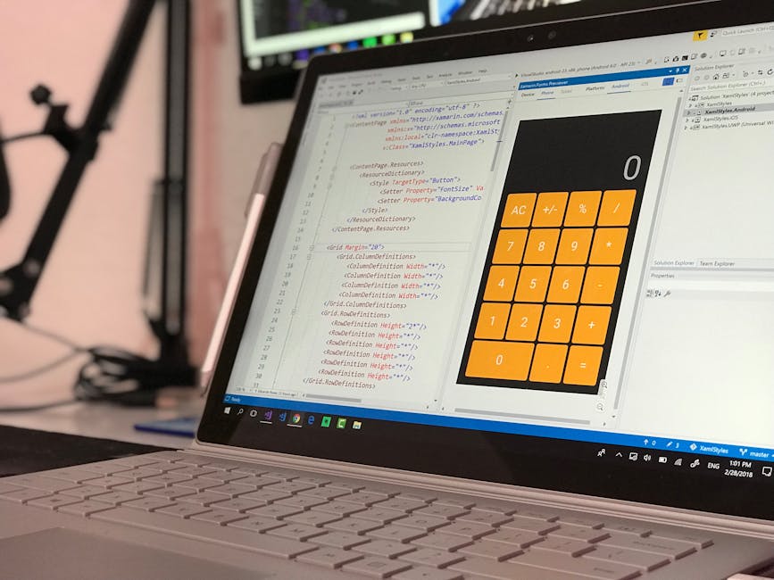 Close-up of a laptop on a desk displaying a coding editor on the left side and a large orange calculator interface on the right side. The coding window contains lines of CSS and HTML code, with some h